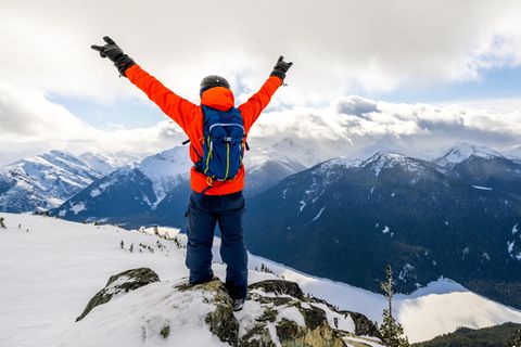 Backpacks für Wintersportler: Mann mit Skirucksack steht auf einem Gipfel mit Blick auf verschneite Berge