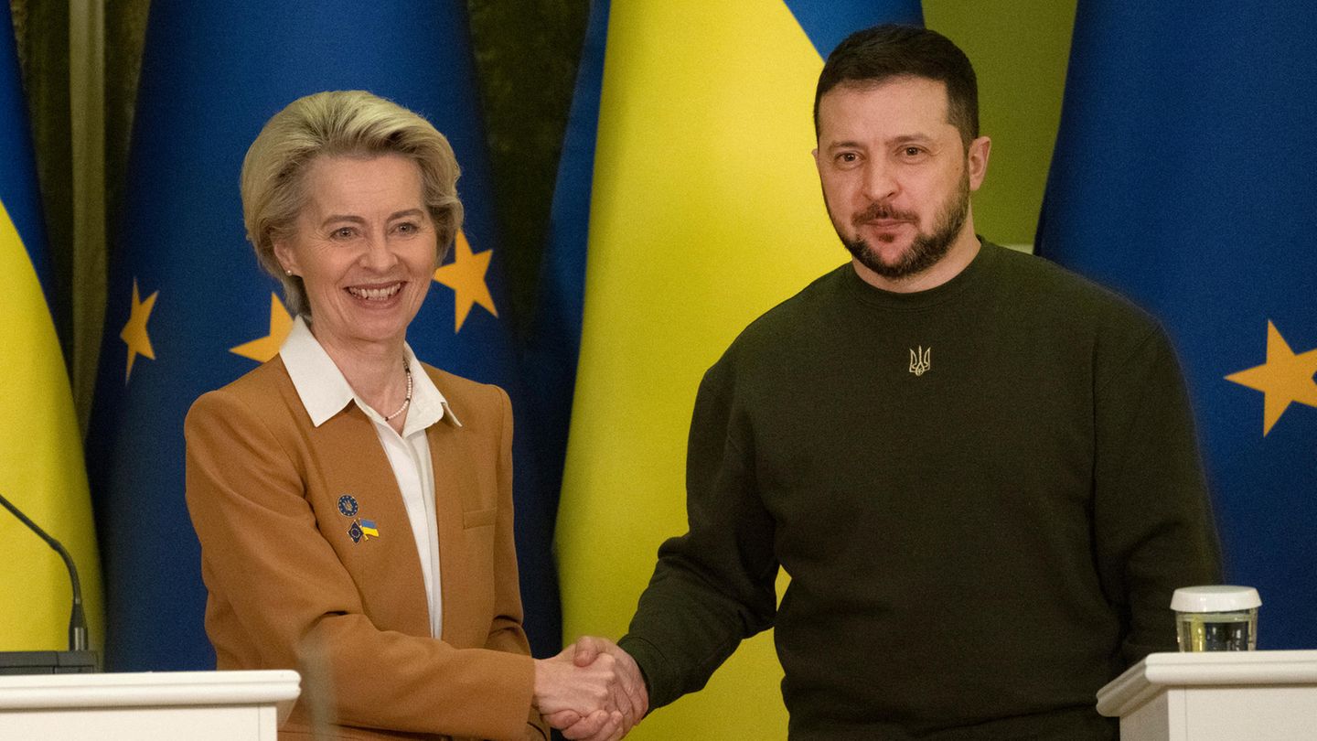 Ursula von der Leyen und Wolodymyr Selenskyj geben einander vor Flaggen der EU und der Ukraine die Hand