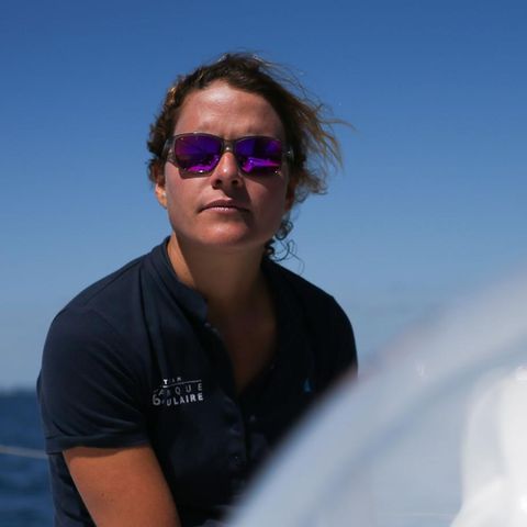 Clarisse Crémer sitzt in blauem Polo-Shirt und mit verspiegelter Sonnenbrille an Bord einer Segeljacht in der Sonne