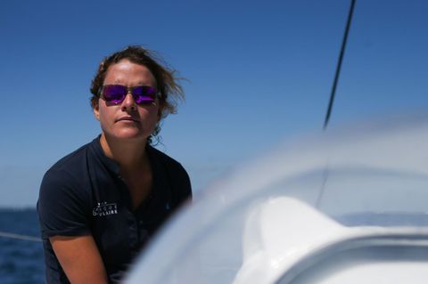 Clarisse Crémer sitzt in blauem Polo-Shirt und mit verspiegelter Sonnenbrille an Bord einer Segeljacht in der Sonne