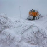 Ein orangefarbener Bagger steht neben den eingeschneiten Gleisen der Schmalspurbahn auf dem Brocken im Schnee