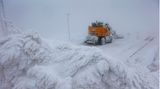 Ein orangefarbener Bagger steht neben den eingeschneiten Gleisen der Schmalspurbahn auf dem Brocken im Schnee