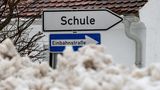 Hinter einem Hügel zusammengeschobenen Schnees ragt ein Wegweiser "Schule" gerade noch so hervor