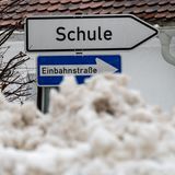 Hinter einem Hügel zusammengeschobenen Schnees ragt ein Wegweiser "Schule" gerade noch so hervor