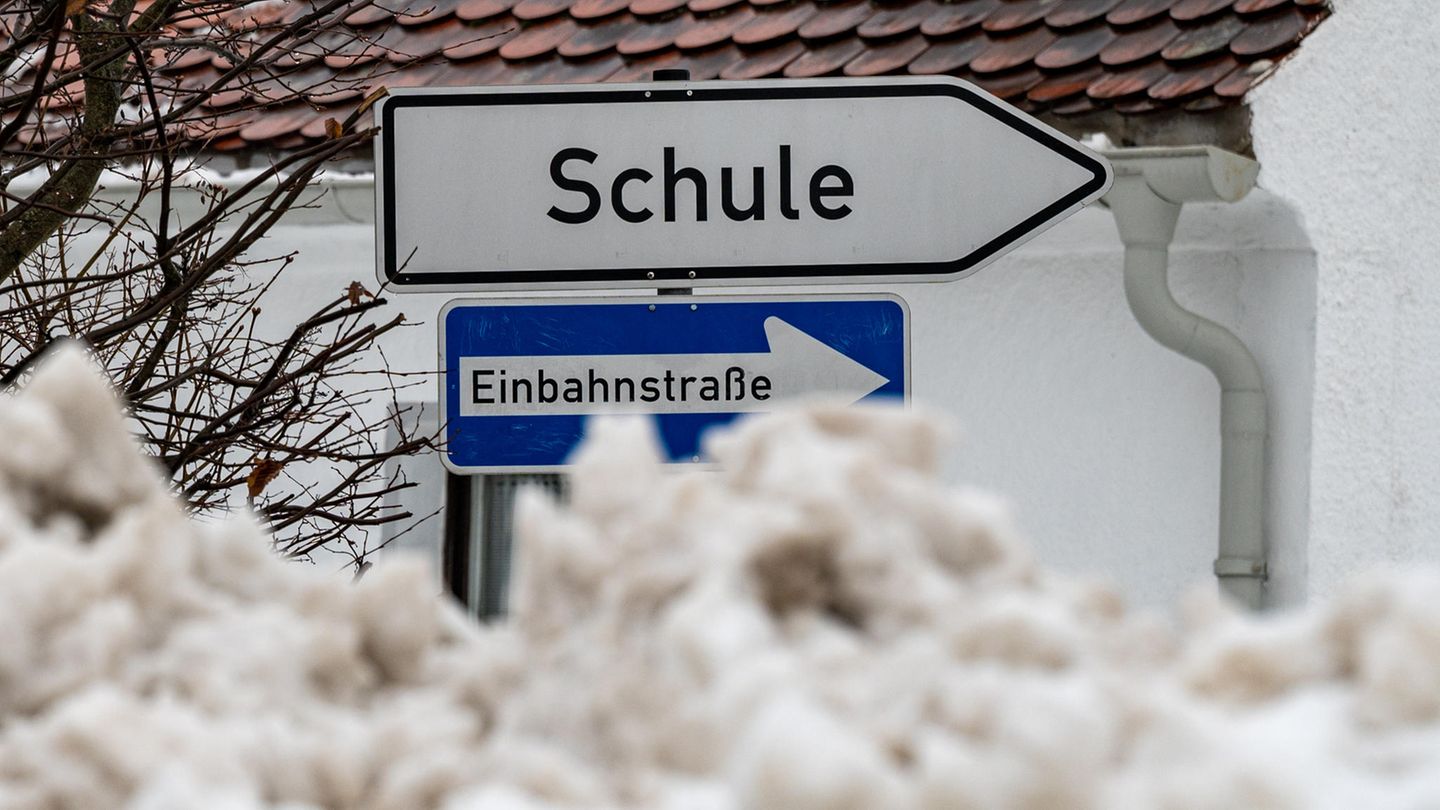 Hinter einem Hügel zusammengeschobenen Schnees ragt ein Wegweiser "Schule" gerade noch so hervor