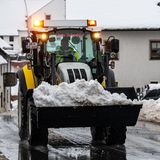 Auf einer nassen Straße fährt ein gelb-schwarzer Radlader mit der Schaufel voller Schnee