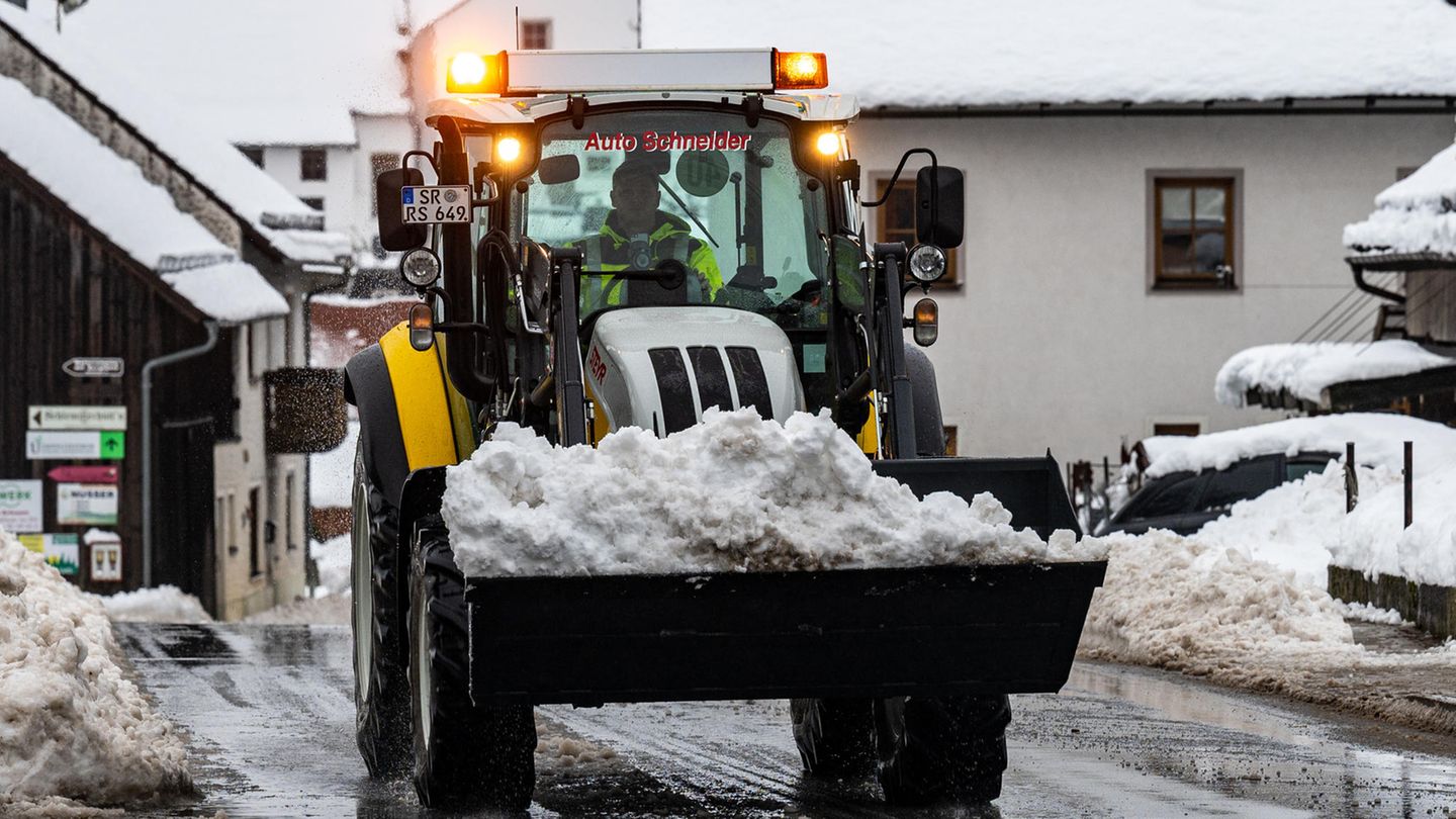 Auf einer nassen Straße fährt ein gelb-schwarzer Radlader mit der Schaufel voller Schnee