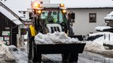 Auf einer nassen Straße fährt ein gelb-schwarzer Radlader mit der Schaufel voller Schnee