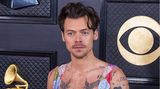 Ausnahmekünstler Harry Styles präsentiert seine Tattoos in einem weit ausgeschnittenen Glitzer-Anzug. 