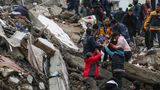 Menschen und Rettungskräfte bergen eine Person auf einer Bahre aus einem eingestürzten Gebäude