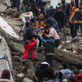 Menschen und Rettungskräfte bergen eine Person auf einer Bahre aus einem eingestürzten Gebäude