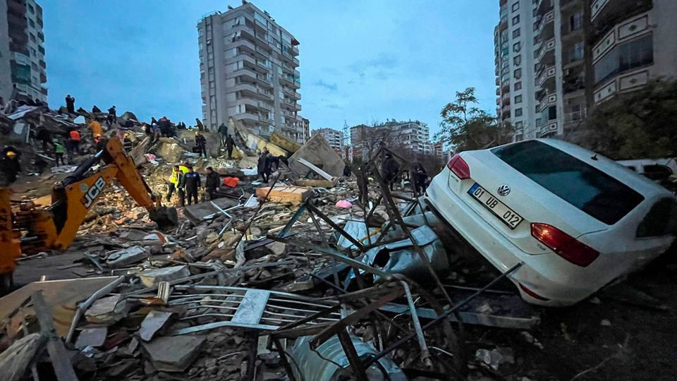 Emergency teams search for people inside a destroyed building while a car lies on the rubble.  After several severe earthquakes in the Turkish-Syrian border region, the death toll continues to rise