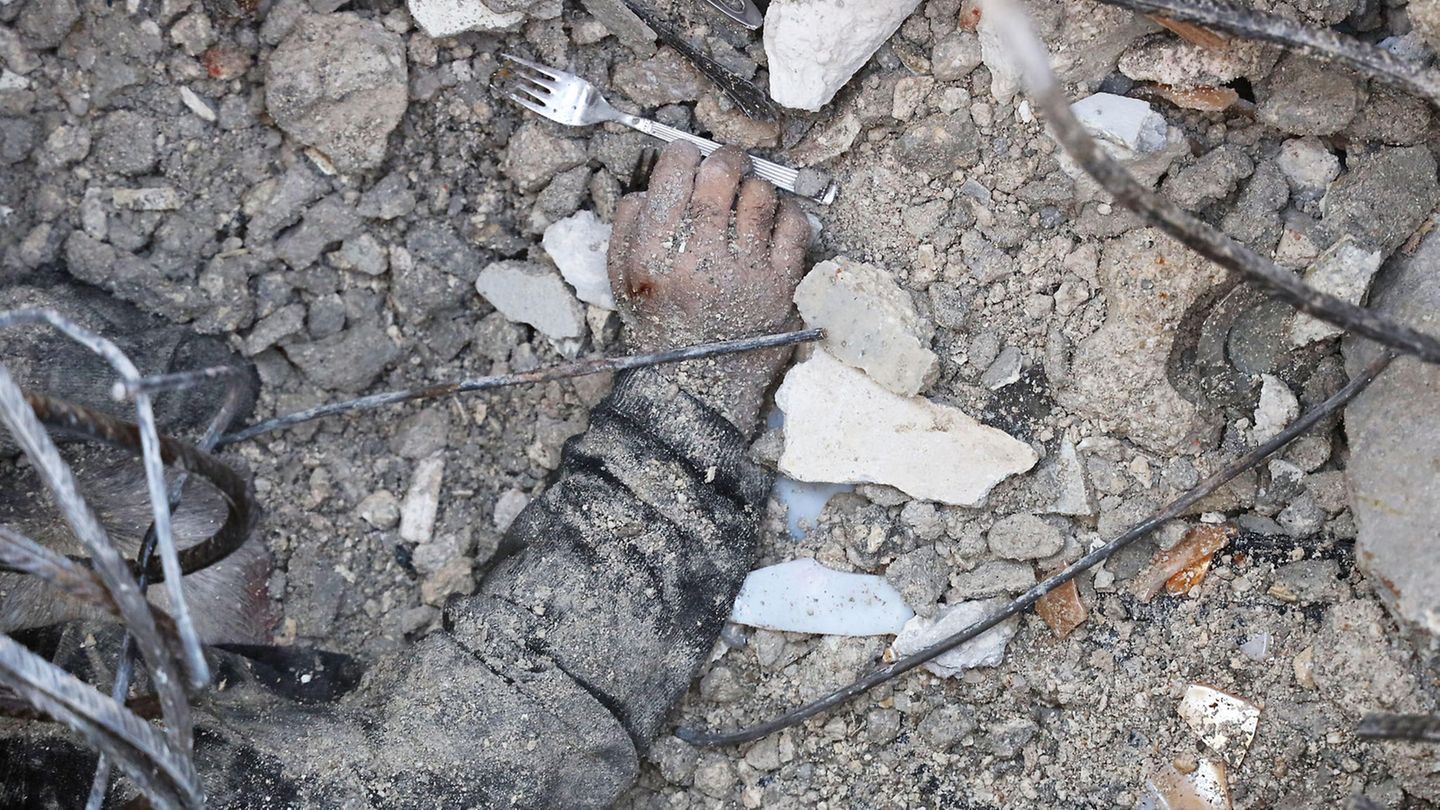 Ein totes Kind liegt mit Staub bedeckt und ausgestreckter Hand auf den Trümmern eines zerstörten Gebäudes