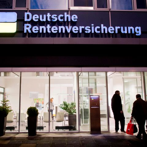 Eine Filiale der Deutschen Rentenversicherung im Dunkeln, davor Menschen