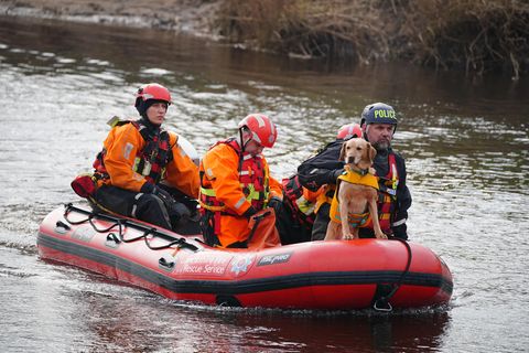 In einem roten Polizei-Schlauchboot auf dem Fluss Wyre sitzen vier Personen in oranger Kleidung. Ein blonder Hund sitzt im Bug