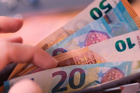 Eine Frau hält ein Portemonnaie in der Hand, in dem Geldscheine stecken