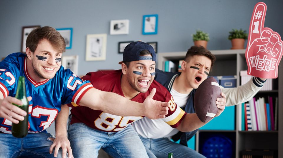 Super Bowl LVII: Drei Footballfans feiern im Wohnzimmer mit Bier und Trikots