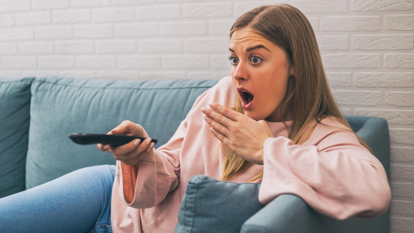 Frau schaut geschockt auf den Fernseher