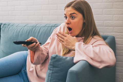 Frau schaut geschockt auf den Fernseher