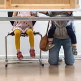 Eine junge Mutter mit zwei Kinder kniet hinter einer Wahlkabine in Berlin