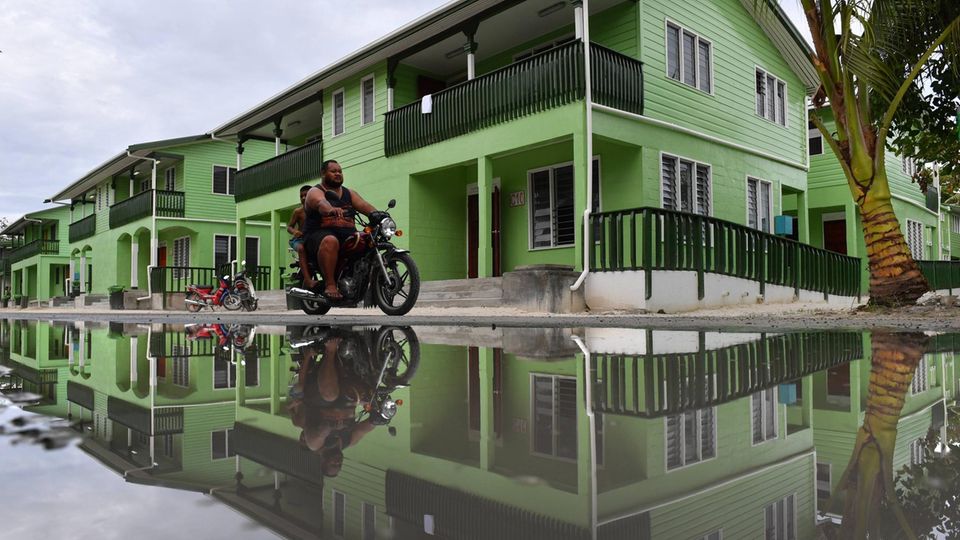 Mann fährt auf einem Motorrad über eine überschwemmte Straße auf Tuvalu