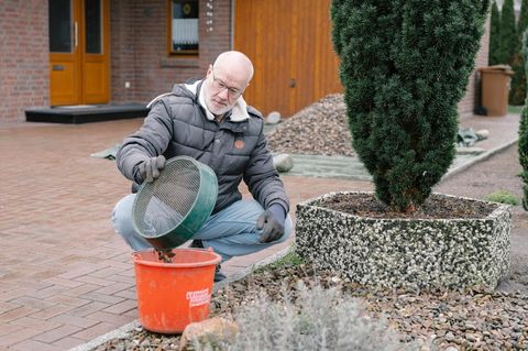 Ein Mann hockt im Schotterbeet