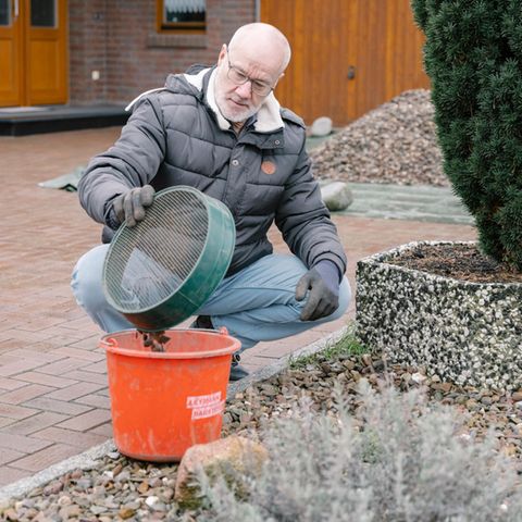 Ein Mann hockt im Schotterbeet