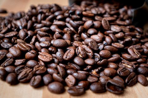 Auf einem Holztisch liegen braun geröstete Kaffeebohnen ausgebreitet