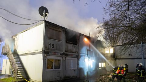 Feuerwehrleute bei Löscharbeiten vor den brennenden Container-Einheiten einer Flüchtlingsunterkunft