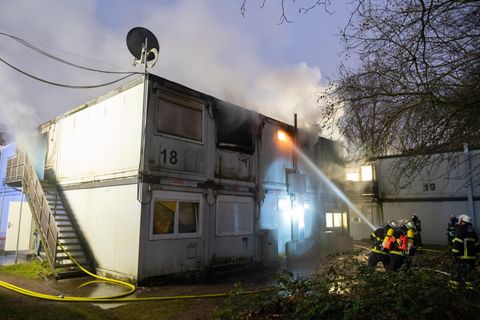 Feuerwehrleute bei Löscharbeiten vor den brennenden Container-Einheiten einer Flüchtlingsunterkunft