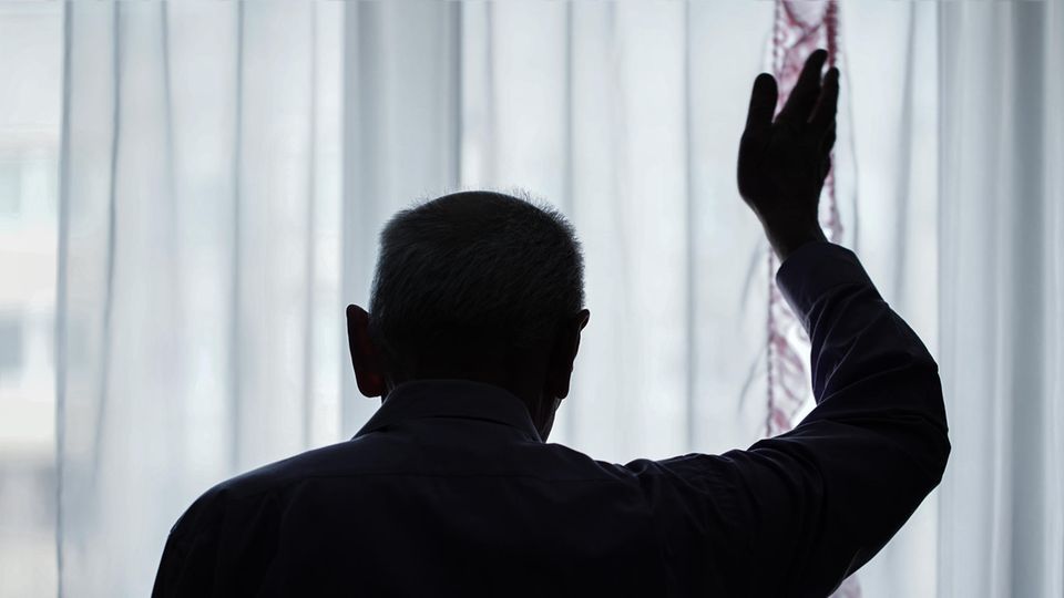 Thema Demenz - Silhouette von älterem Herrn mit winkender Hand am Fenster