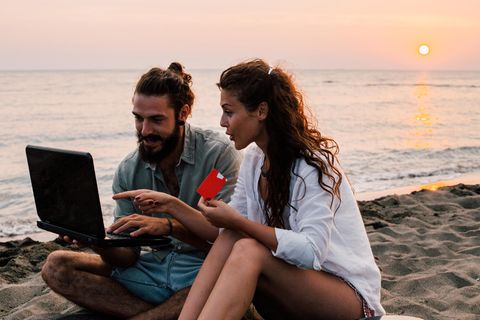 Paar am Strand mit Laptop und Kreditkarte