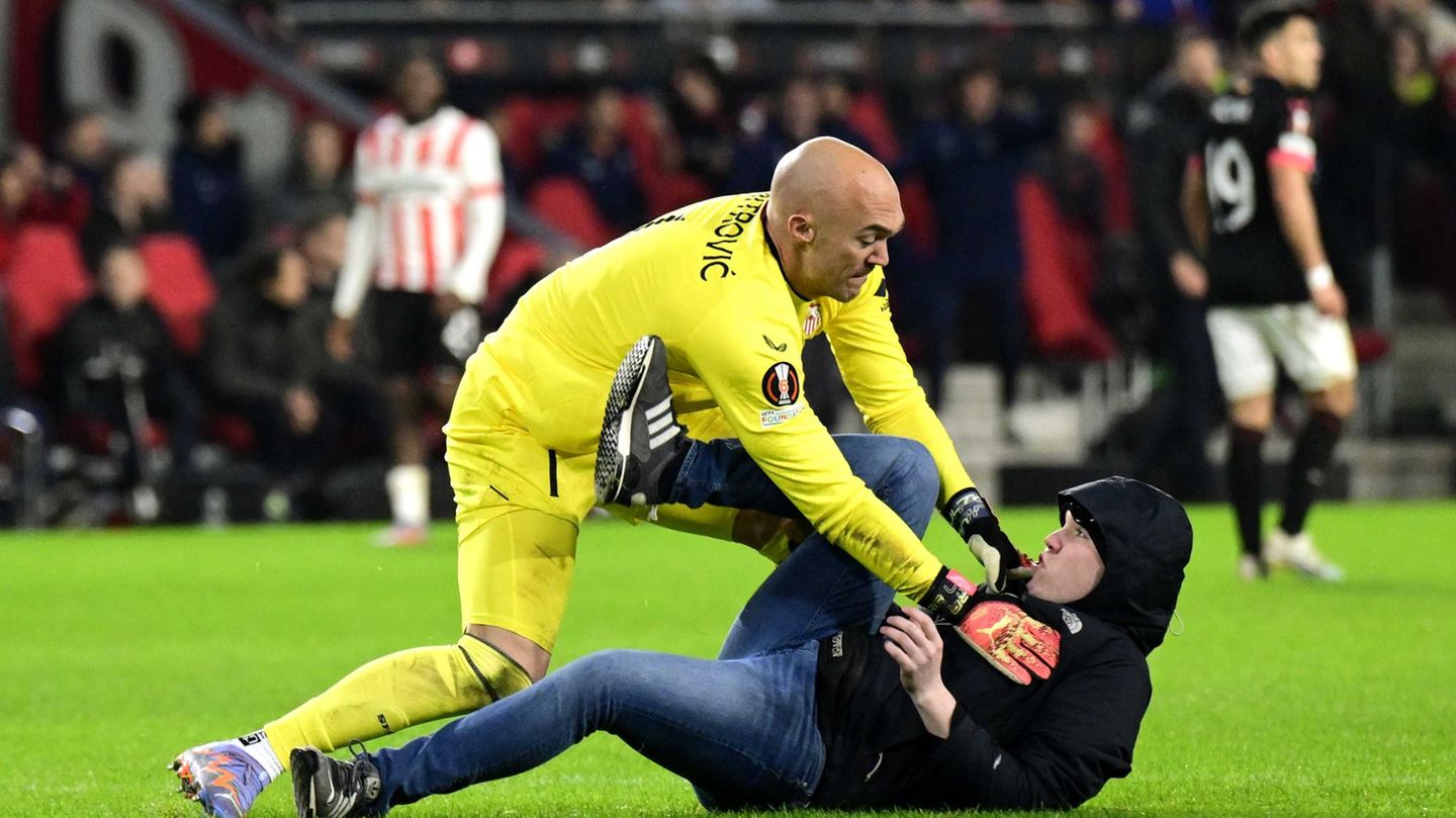 Europa League: Torwart Dmitrovic kann den Angreifer überwältigen, der ihm zuvor mit der Faust ins Gesicht geschlagen hat. Mutmaßlich ist der Fan wütend darüber, dass sein Team kurz vor dem Aus in der Europa League steht. Zum Zeitpunkt des Angriffs führt Eindhoven zwar mit 1:0, aber das ist zu wenig angesichts des 3:0-Sieges Sevillas im Hinspiel. Torwart Dmitrovic kann den Angreifer überwältigen, der ihm zuvor mit der Faust ins Gesicht geschlagen hat. Mutmaßlich ist der Fan wütend darüber, dass sein Team kurz vor dem Aus in der Europa League steht. Zum Zeitpunkt des Angriffs führt Eindhoven zwar mit 1:0, aber das ist zu wenig angesichts des 3:0-Sieges Sevillas im Hinspiel.