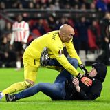 Torwart Dmitrovic kann den Angreifer überwältigen, der ihm zuvor mit der Faust ins Gesicht geschlagen hat. Mutmaßlich ist der Fan wütend darüber, dass sein Team kurz vor dem Aus in der Europa League steht. Zum Zeitpunkt des Angriffs führt Eindhoven zwar mit 1:0, aber das ist zu wenig angesichts des 3:0-Sieges Sevillas im Hinspiel.