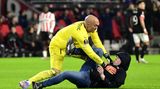 Torwart Dmitrovic kann den Angreifer überwältigen, der ihm zuvor mit der Faust ins Gesicht geschlagen hat. Mutmaßlich ist der Fan wütend darüber, dass sein Team kurz vor dem Aus in der Europa League steht. Zum Zeitpunkt des Angriffs führt Eindhoven zwar mit 1:0, aber das ist zu wenig angesichts des 3:0-Sieges Sevillas im Hinspiel.