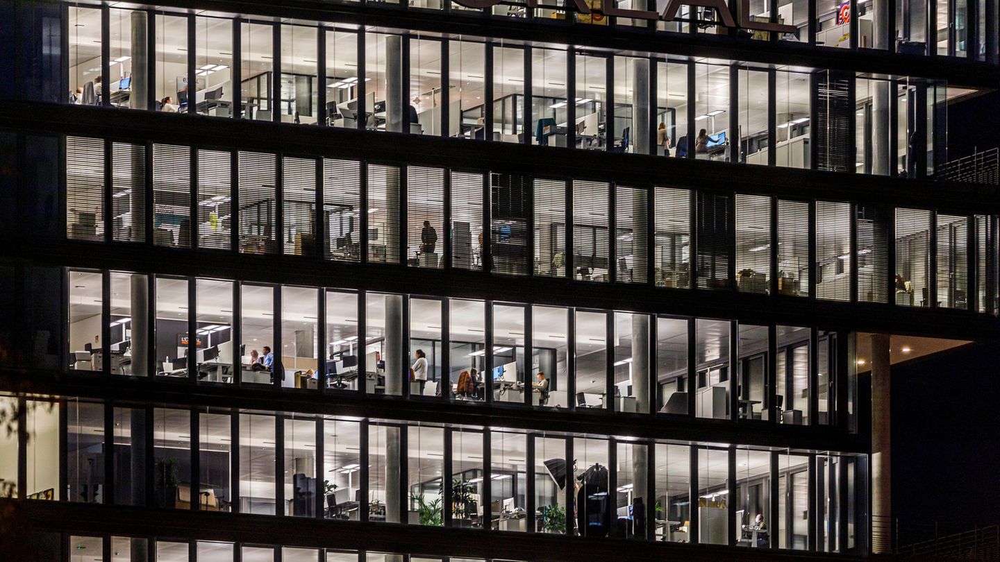 Debatte um Arbeitszeit: Ein Großraumbüro am Abend. Draußen ist es dunkel, drinnen beleuchtet.
