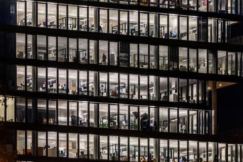 Debatte um Arbeitszeit: Ein Großraumbüro am Abend. Draußen ist es dunkel, drinnen beleuchtet.