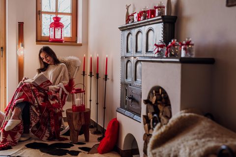 Junge Frau sitze an Kachelofen und liest ein Buch