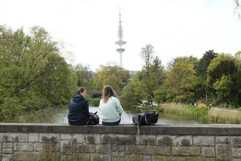 Frauen sitzen zum Frühlingsanfang auf einer Mauer vor der Parkanlage Planten un Blomen