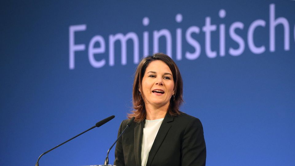 Annalena Baerbock steht vor einer blauen Wand, an der in hellblau das Wort "Feministisch" steht