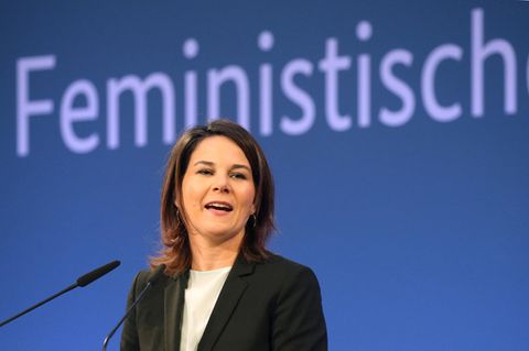 Annalena Baerbock steht vor einer blauen Wand, an der in hellblau das Wort "Feministisch" steht