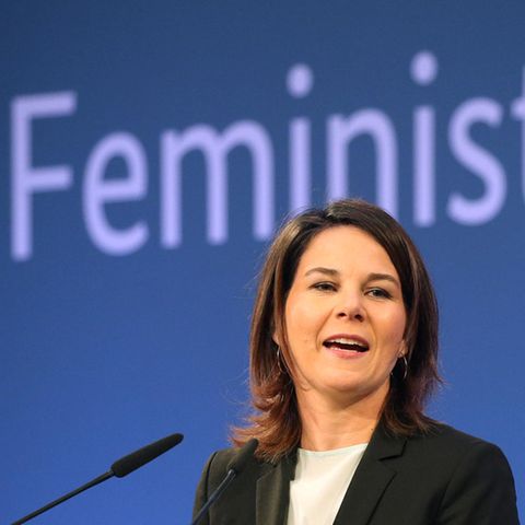 Annalena Baerbock steht vor einer blauen Wand, an der in hellblau das Wort "Feministisch" steht