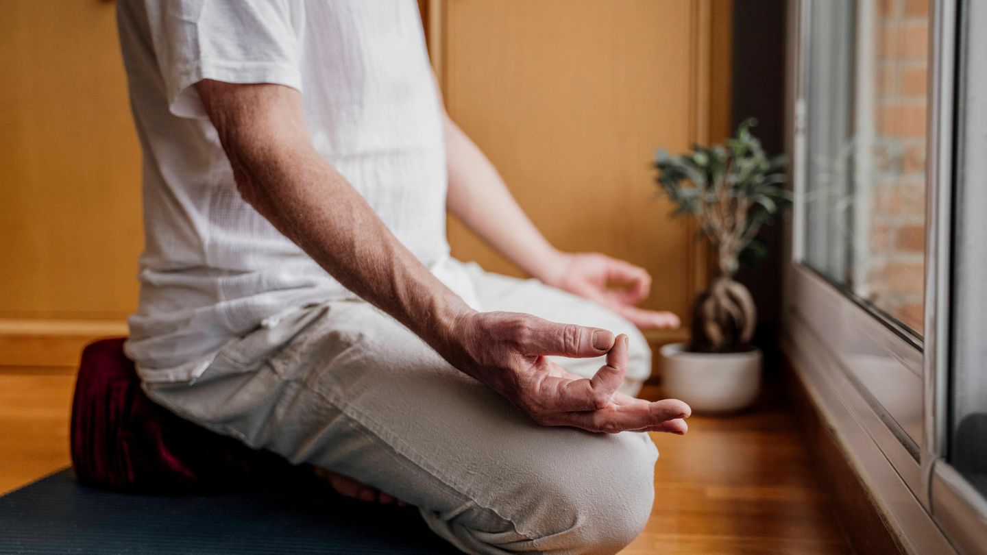 Mann sitzt im Schneidersitz auf einem Yoga-Kissen