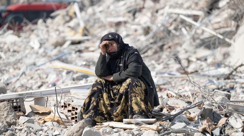 Eine Frau sitzt nach dem Beben in der Türkei und in Syrien in der Stadt Antakya zwischen Trümmern.