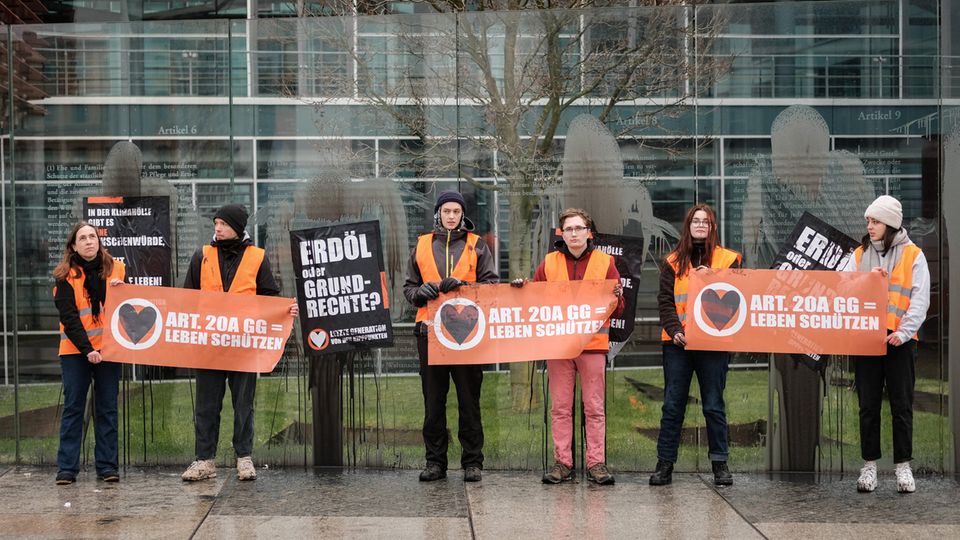Aktivisten der Letzten Generation halten Protestschilder vor dem Grundgesetz-Denkmal in die Höhe