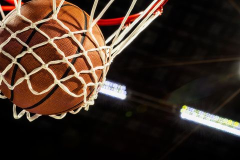 Ein Basketball fällt gerade durchs Netz eines Korbes in einer Sporthalle