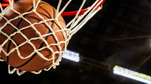 Ein Basketball fällt gerade durchs Netz eines Korbes in einer Sporthalle