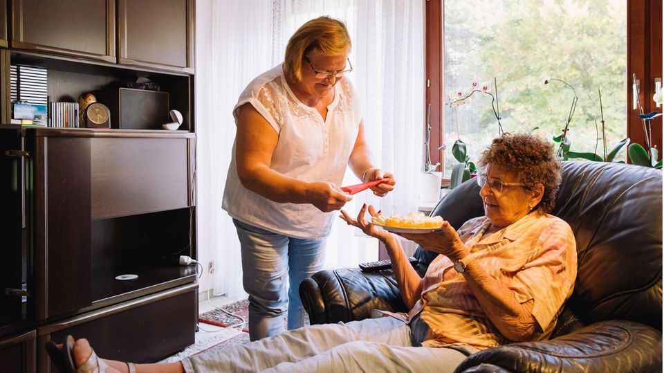 Pflegerin Małgorzata K. reicht der Seniorin Brigitte M., die auf einem Liegesessel sitzt, eine Serviette