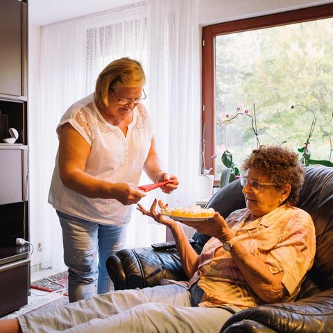 Pflegerin Małgorzata K. reicht der Seniorin Brigitte M., die auf einem Liegesessel sitzt, eine Serviette