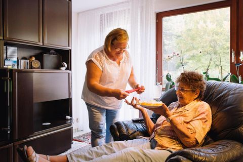 Pflegerin Małgorzata K. reicht der Seniorin Brigitte M., die auf einem Liegesessel sitzt, eine Serviette